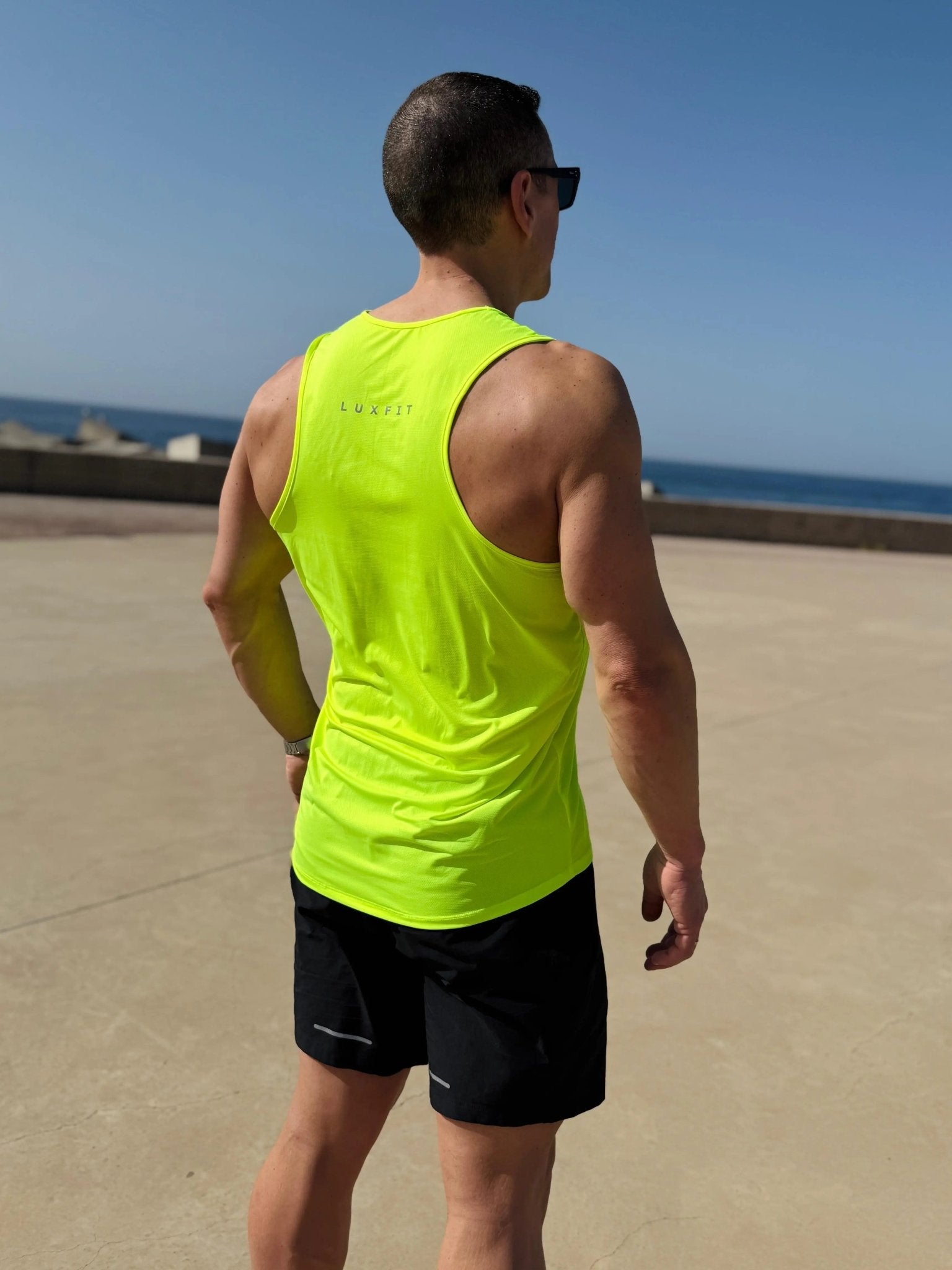 Hombre de espaldas en el exterior vistiendo la camiseta técnica sin mangas MAN-U de LUXFEEL en color Amarillo, diseñada para un alto rendimiento.