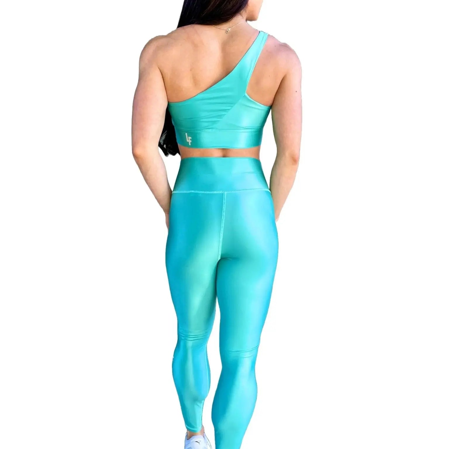 Mujer vistiendo el conjunto azul celeste brillante de LUXFEEL, compuesto por el top asimétrico Carmela (un solo hombro y apertura en el escote) y el legging Pearl Shine a juego.