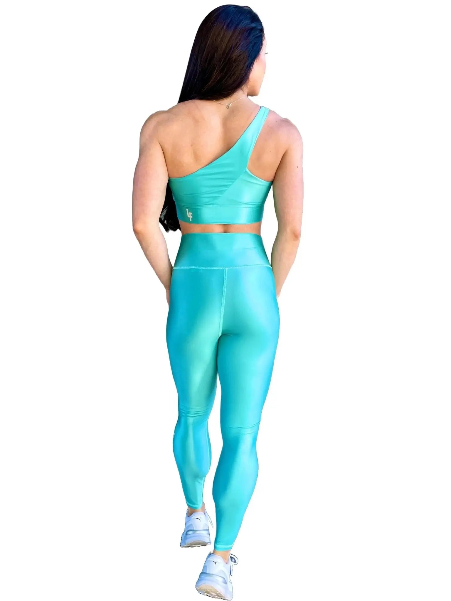 Mujer vistiendo el conjunto azul celeste brillante de LUXFEEL, compuesto por el top asimétrico Carmela (un solo hombro y apertura en el escote) y el legging Pearl Shine a juego.