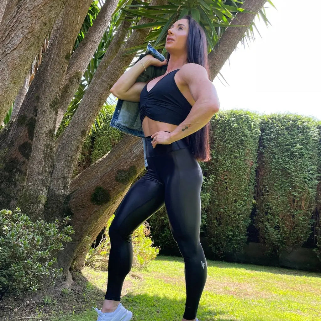 Mujer vistiendo los leggings brillantes de cintura alta Legging Pearl Shine de LUXFEEL en color Negro Brillante, con acabado efecto perla.