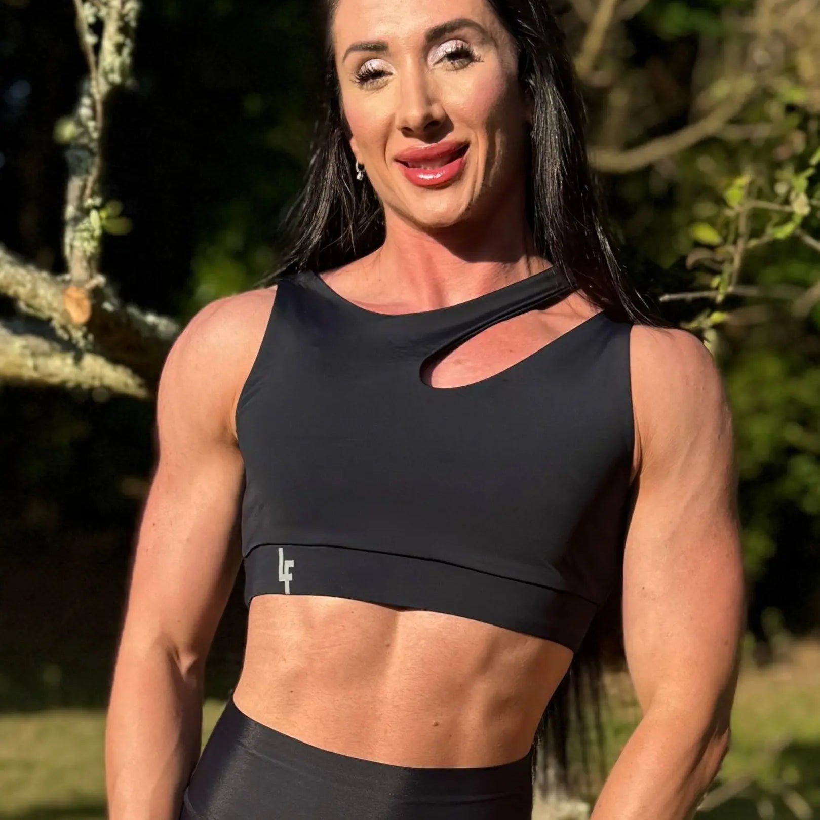 Modelo en la naturaleza mostrando Top Vanesa (foto de frente) de LUXFEEL en color negro, con un diseño de apertura en el hombro y soporte extra.