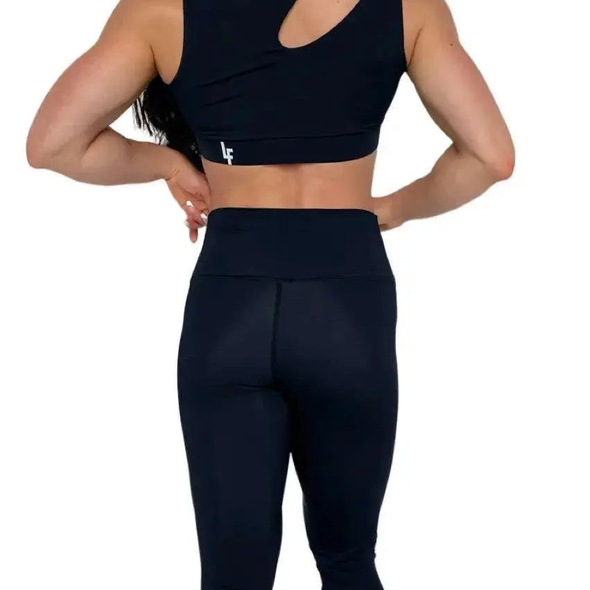 Mujer luciendo el top asimétrico Top Vanesa de LUXFEEL en color Negro, con un diseño de apertura en el hombro y soporte extra.