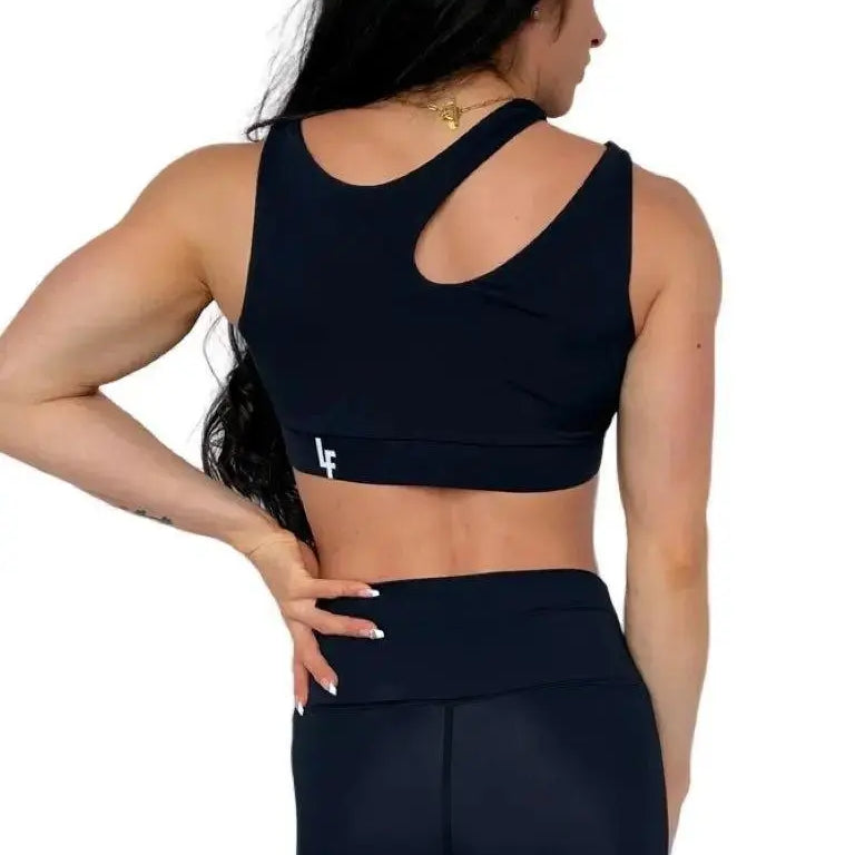 Mujer luciendo el top asimétrico Top Vanesa de LUXFEEL en color Negro, con un diseño de apertura en el hombro y soporte extra.