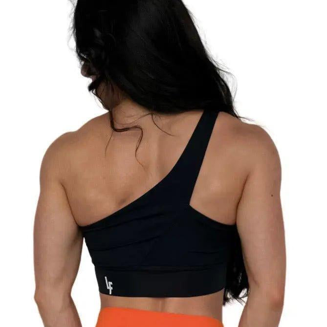 Mujer luciendo el top asimétrico Top Carmela de LUXFEEL en color Negro, con diseño de un solo hombro y apertura en el escote