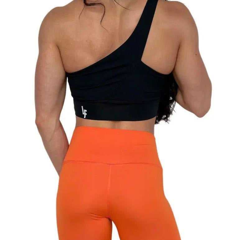 Mujer luciendo el top asimétrico Top Carmela de LUXFEEL en color Negro, con diseño de un solo hombro y apertura en el escote