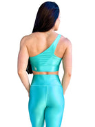 Mujer vistiendo el conjunto azul celeste brillante de LUXFEEL, compuesto por el top asimétrico Carmela (un solo hombro y apertura en el escote) y el legging Pearl Shine a juego.