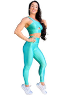 Mujer vistiendo el conjunto azul celeste brillante de LUXFEEL, compuesto por el top asimétrico Carmela (un solo hombro y apertura en el escote) y el legging Pearl Shine a juego.