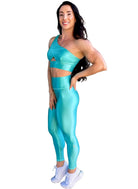 Mujer vistiendo el conjunto azul celeste brillante de LUXFEEL, compuesto por el top asimétrico Carmela (un solo hombro y apertura en el escote) y el legging Pearl Shine a juego.