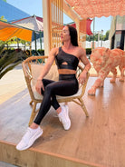 Mujer luciendo el top asimétrico brillante Top Carmela Pearl Shine de LUXFEEL en color Negro Brillante, con diseño de un solo hombro y apertura en el escote.