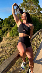 Modelo con el conjunto Negro - Top Carmela y Short Cintura Alta de LUXFEEL apoyada en un pasamanos