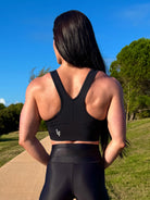 Mujer vistiendo el crop top deportivo Top Adela (de espaldas) de LUXFEEL en color Negro, con escote en V y detalle fruncido en el pecho.