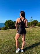 Mujer vistiendo el crop top deportivo Top Adela (posando de espaldas en el campo) de LUXFEEL en color Negro, con escote en V y detalle fruncido en el pecho.