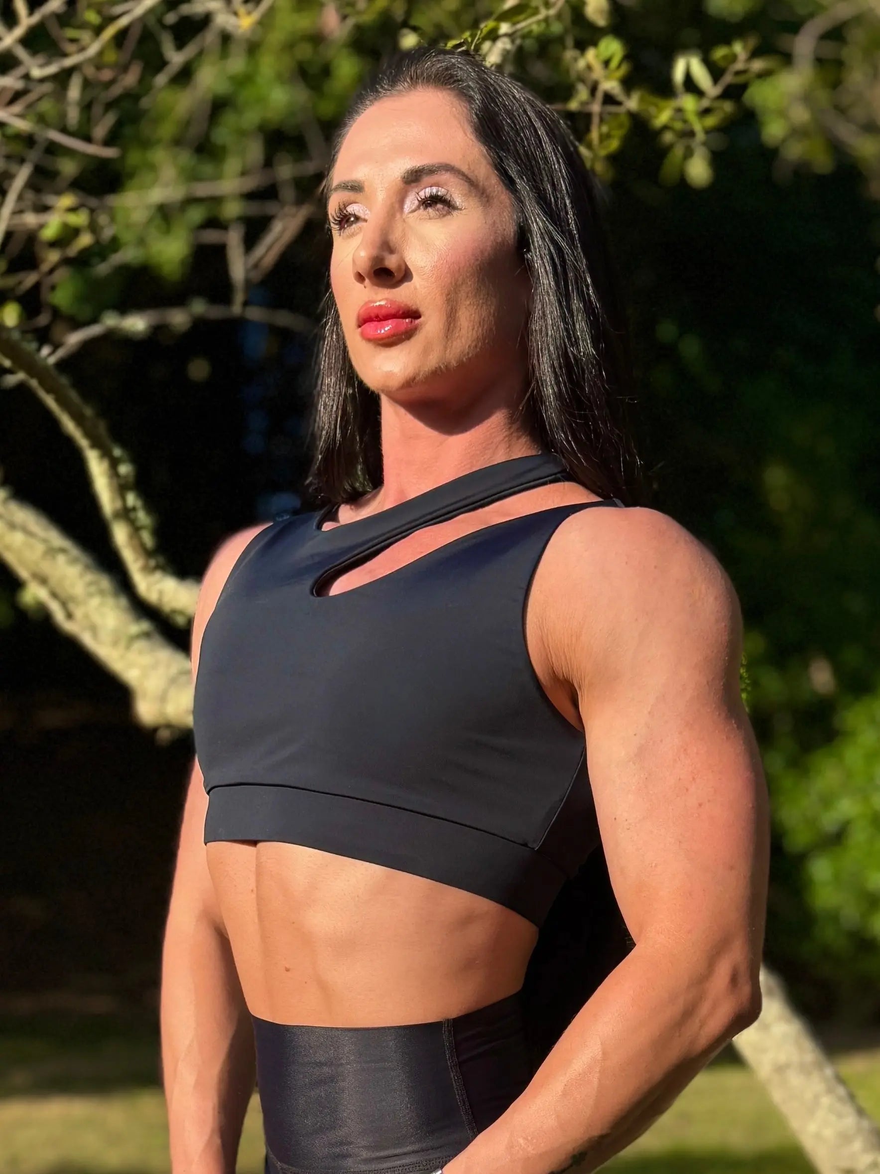 Modelo en la naturaleza mostrando Top Vanesa (foto retrato) de LUXFEEL en color negro,  con un diseño de apertura en el hombro y soporte extra.